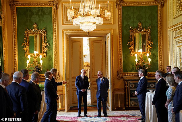 John Kerry (left with his hand raised) speaks to Joe Biden and King Charles below a chandelier inside Windsor Castle
