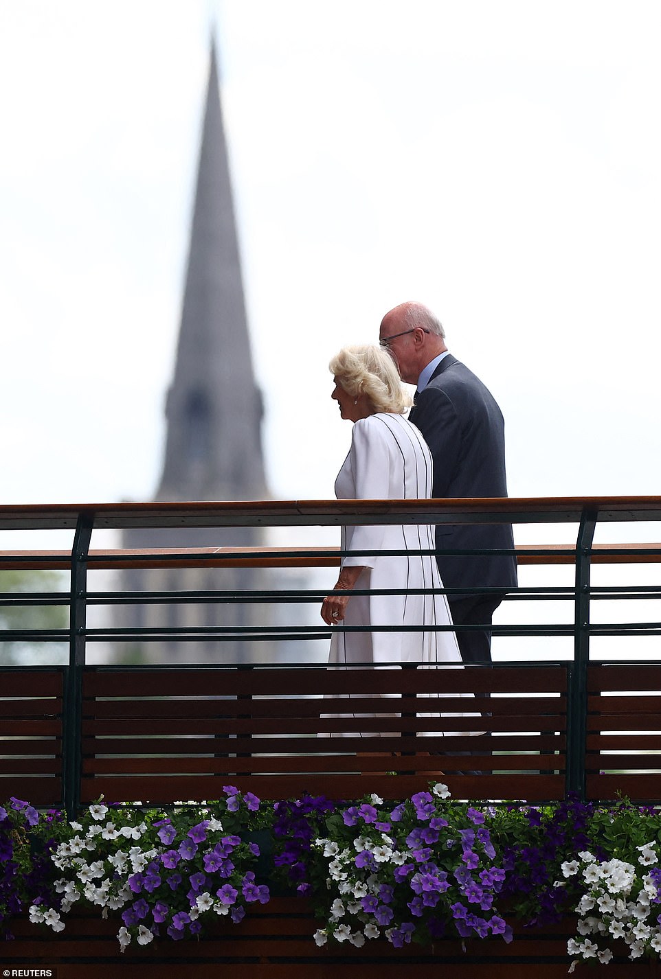 With Wimbledon's church spire in the background, Queen Camilla makes her way across the famous bridge to reach Centre Court
