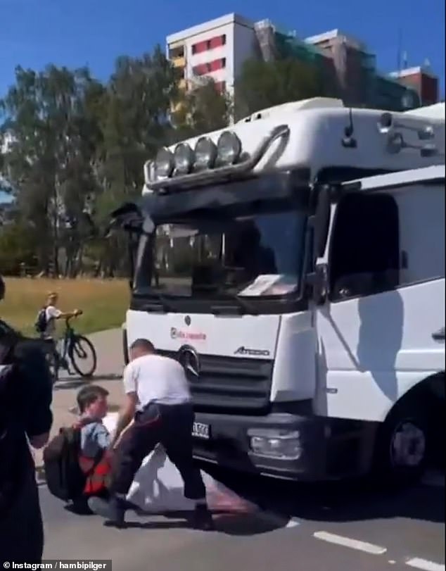 Auf dem Bild ist der Fahrer zu sehen, der versucht, den auf der Straße sitzenden Demonstranten unter dem Lastwagen hervorzuziehen