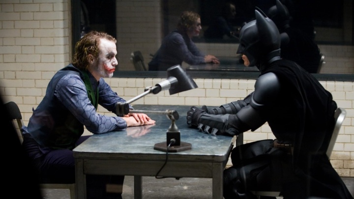 Der Joker und Batman sitzen sich an einem Tisch gegenüber.