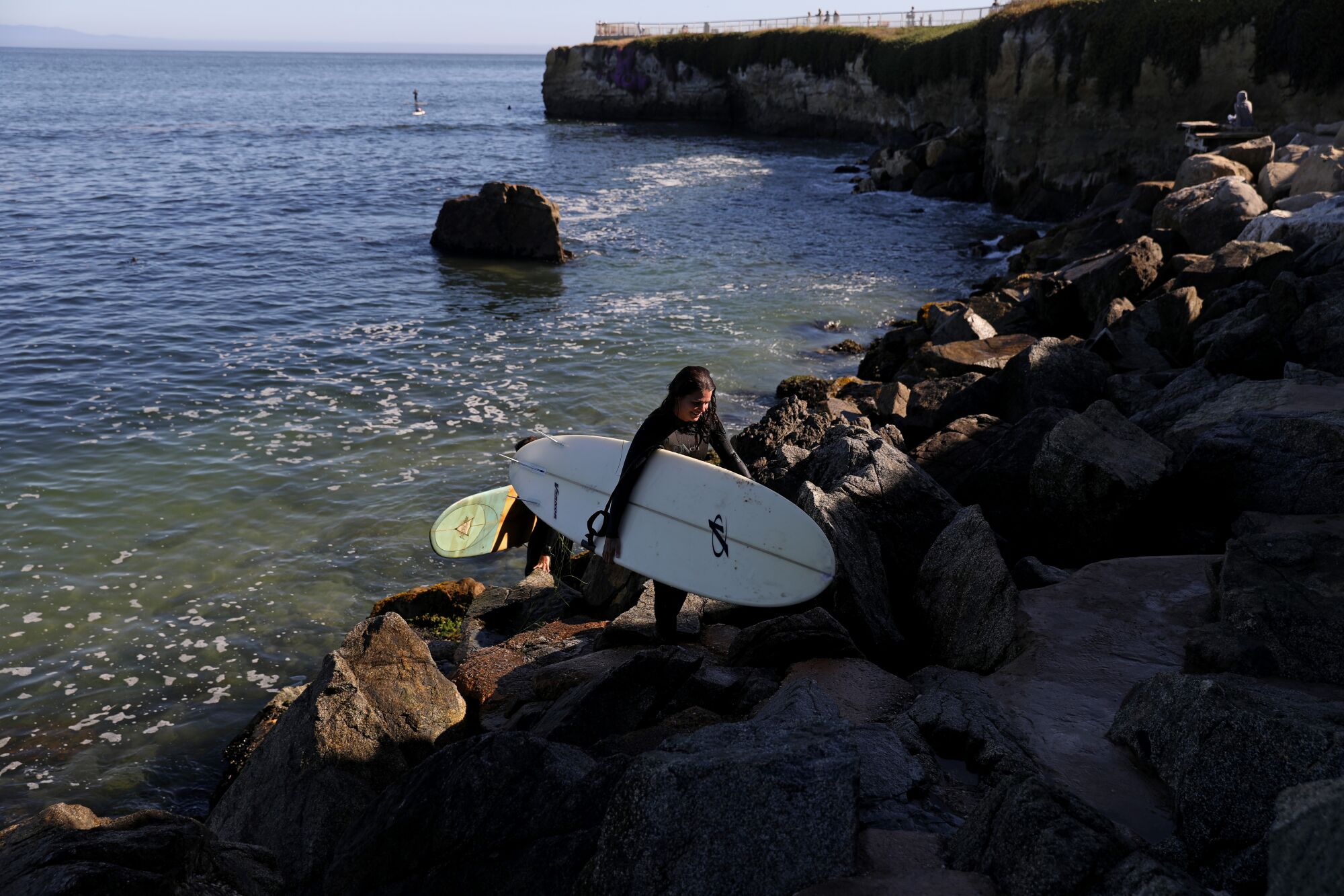 Ein Surfer mit einem Whiteboard geht einen felsigen Abhang hinauf 