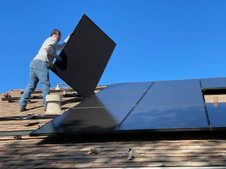 Ein Mann installiert eine Solaranlage auf dem Dach eines Hauses.