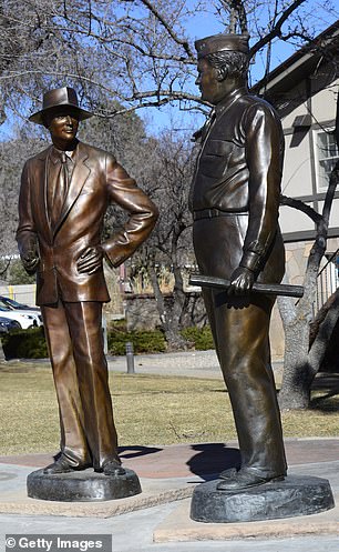 Two bronze sculptures of Dr. J. Robert Oppenheimer and General Leslie Groves stand in a park in the city