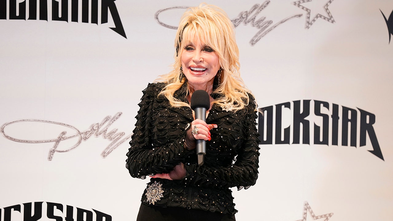Dolly Parton in a black outfits laughs while she holds a microphone at the Dolly! All Access Pop-Up Store in Texas
