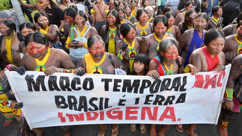 Indigene Menschen in Gesichtsbemalung und traditioneller Kleidung marschieren mit einem Banner mit der Aufschrift: "Marco temporal"