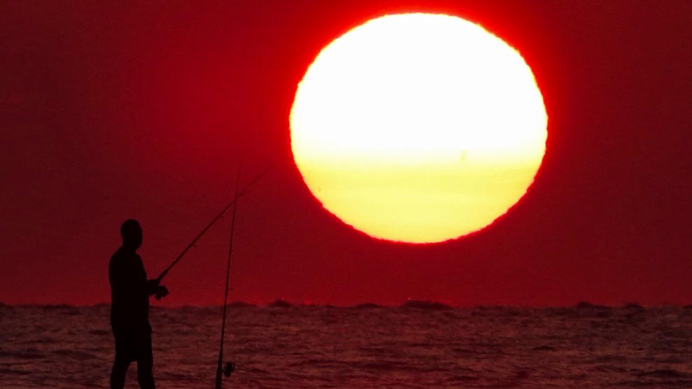 Die Silhouette eines Fischers vor einem dramatischen Sonnenaufgang, der als riesiger Ball über dem Strand erscheint, 12. Juli 2023 in Isle of Palms, South Carolina.  Der Himmel ist rot.