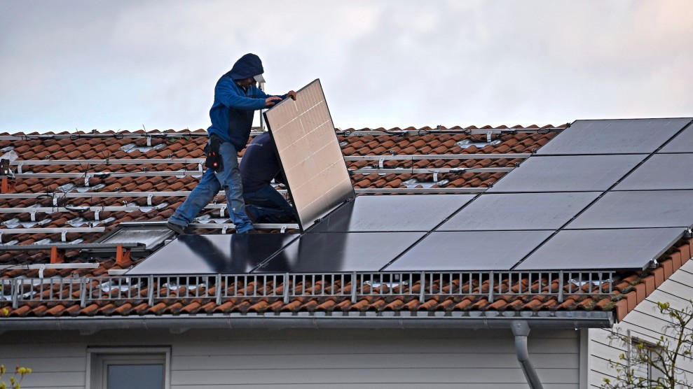 Ein Arbeiter in Jeans und Jacke installiert Sonnenkollektoren auf einem roten Hausdach.