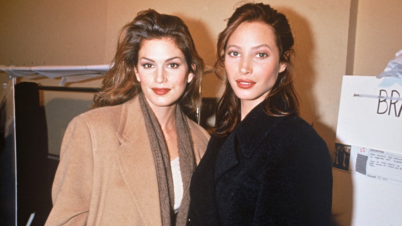 Cindy Crawford in a tan coat soft smiles with Christy Turlington in a black coat at a Chanel fashion show in Paris