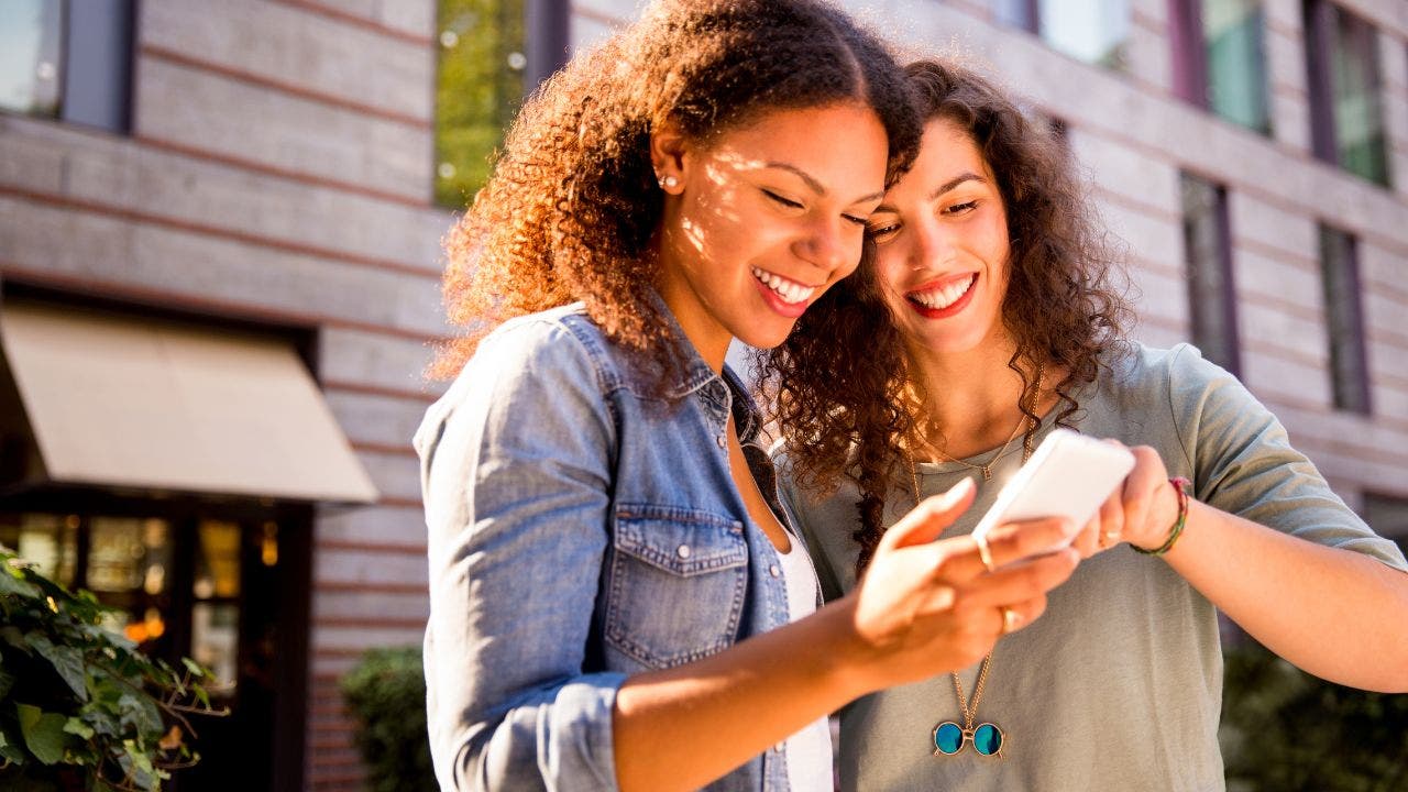 Two women smile as they look at a phone