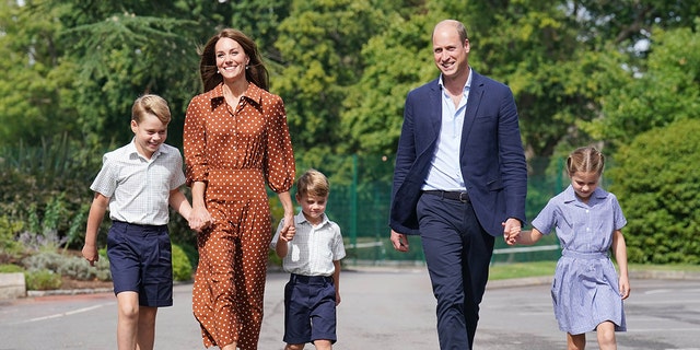Kate Middleton in a polka dot brown dress walking alongside Prince William and their three children as they wear various shades of blue and white