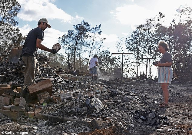 Brook Cretton (L) holds a stack of dishes that he salvaged from the rubble of a home that was destroyed by wildfire on August 12