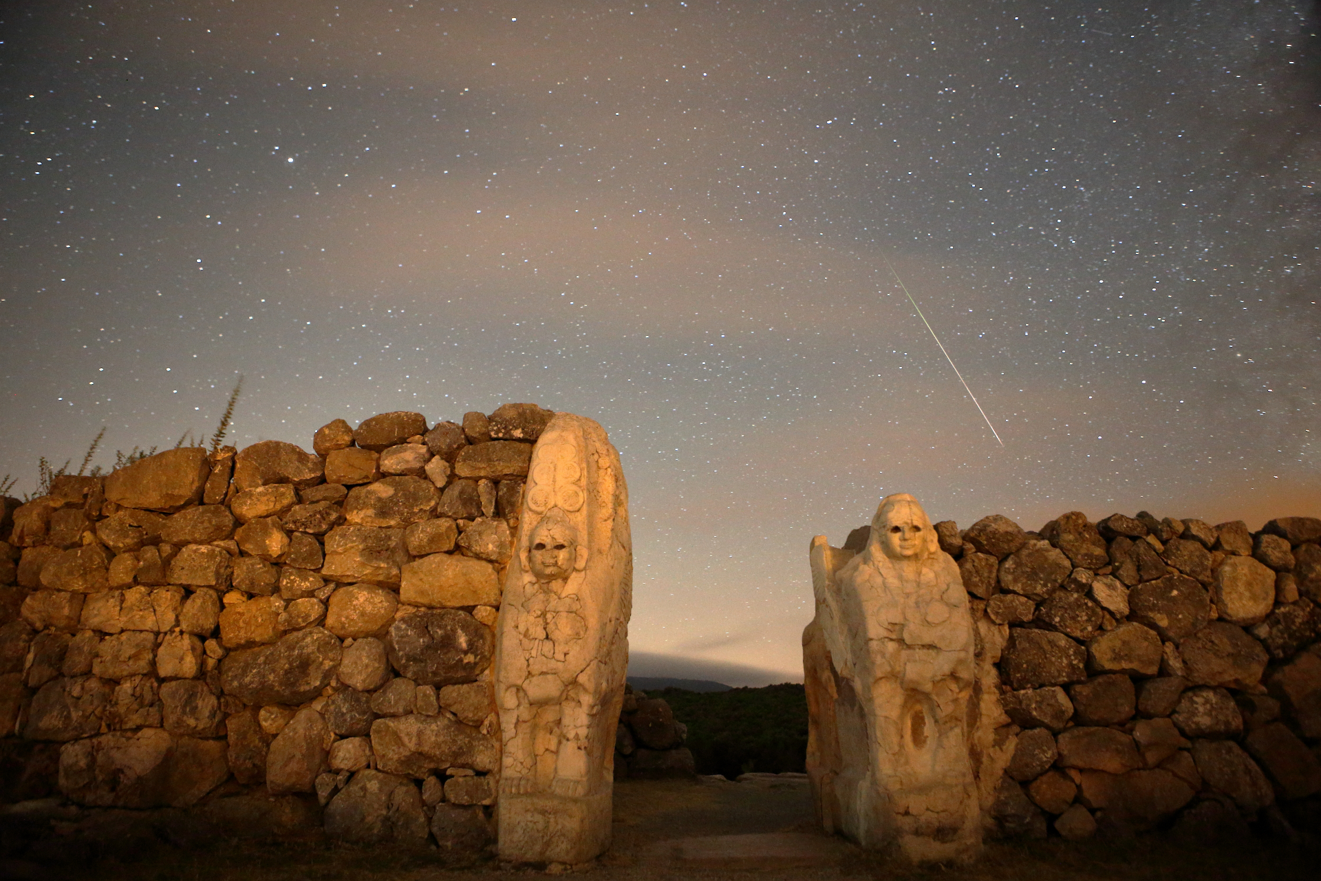 Perseiden-Meteorstreifen am Himmel über einer Steinmauer mit zwei in den Fels gehauenen Figuren.