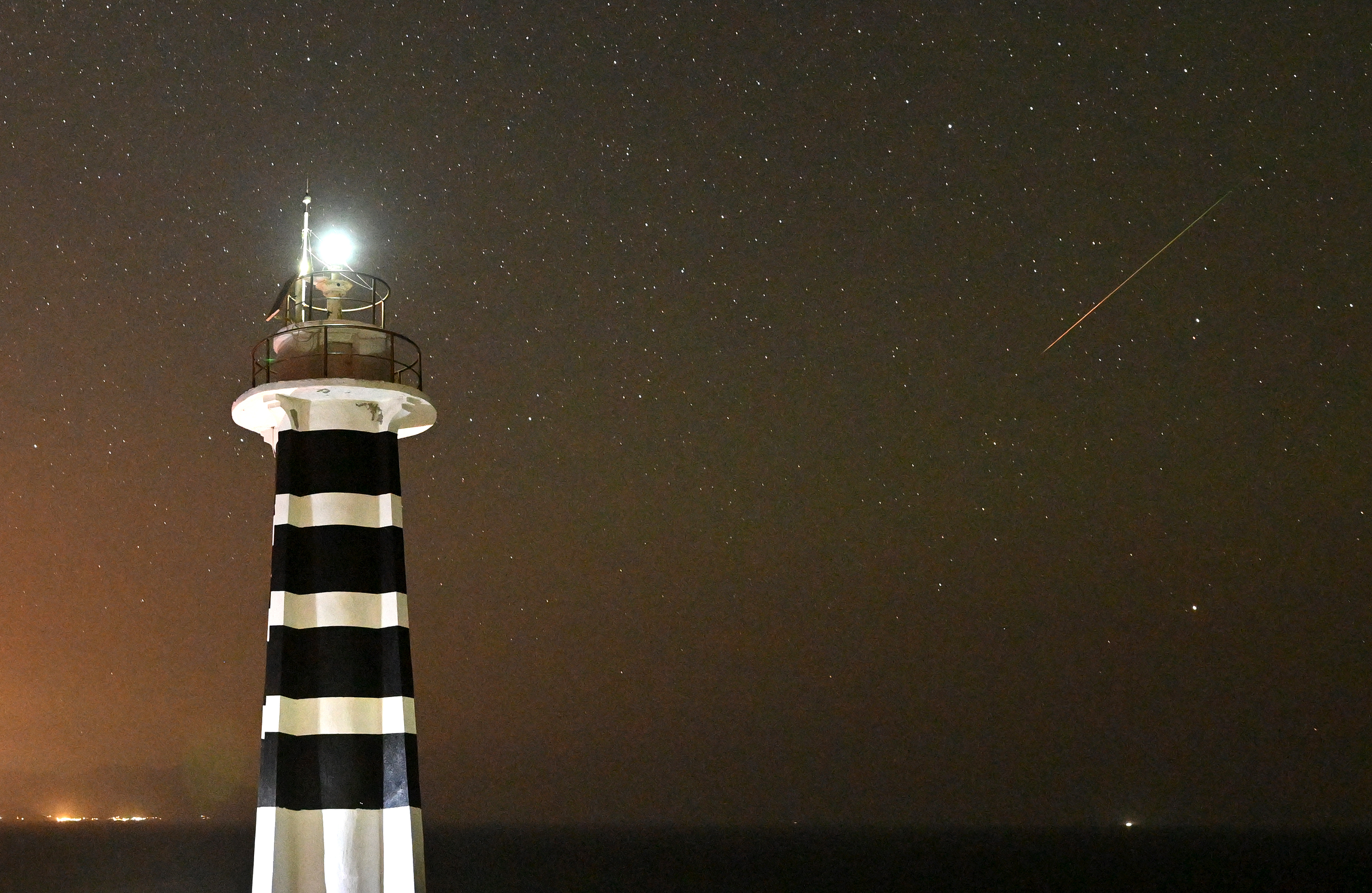 Rechts ein Perseiden-Meteor und links ein heller, schwarz-weiß gestreifter Leuchtturm.