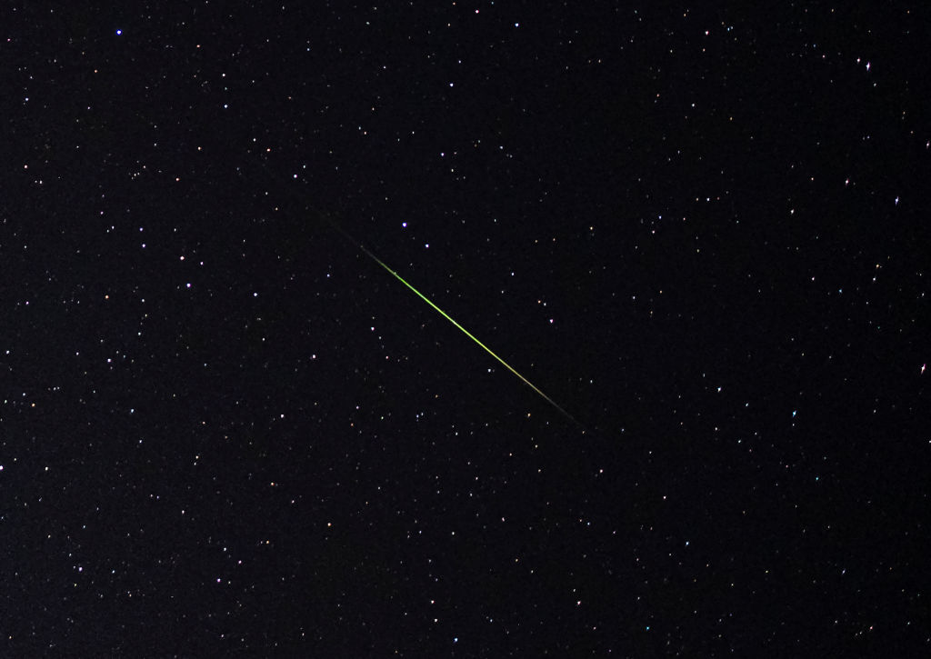 Eine Nahaufnahme eines leuchtend grünen und weißen Perseiden-Meteorstreifens durch den sternenübersäten Himmel.