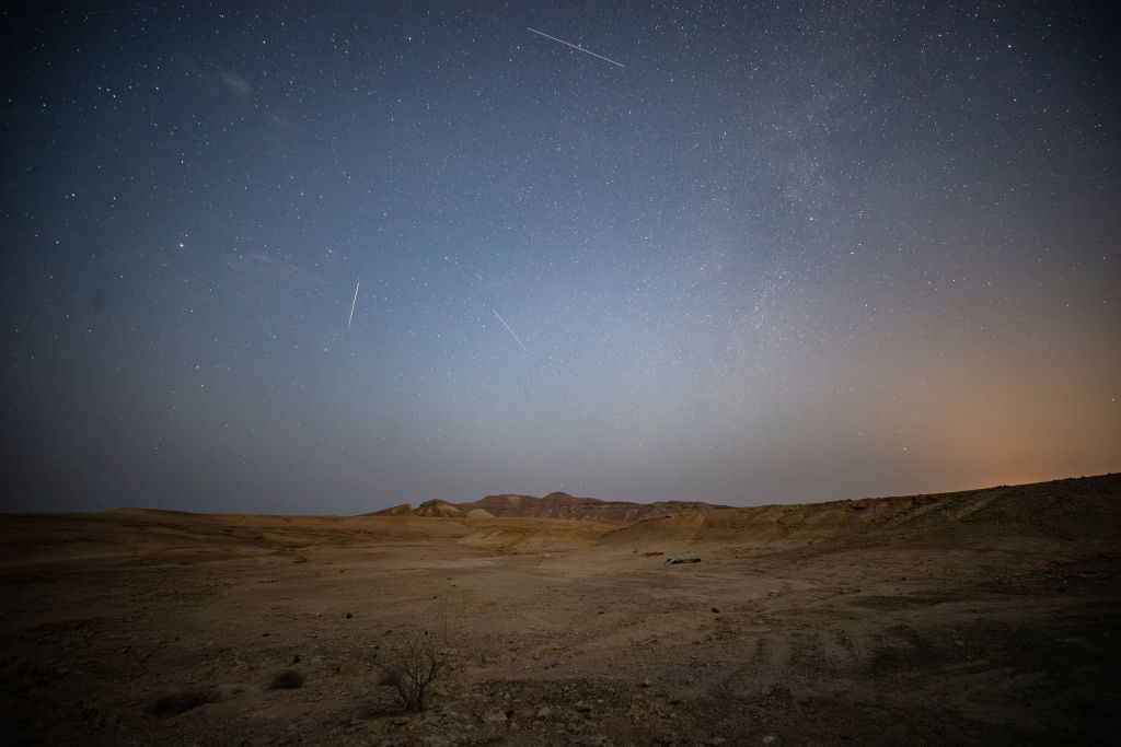 Zahlreiche perseidische Meteore streifen über den sternenübersäten Himmel über einer kargen Wüstenlandschaft.