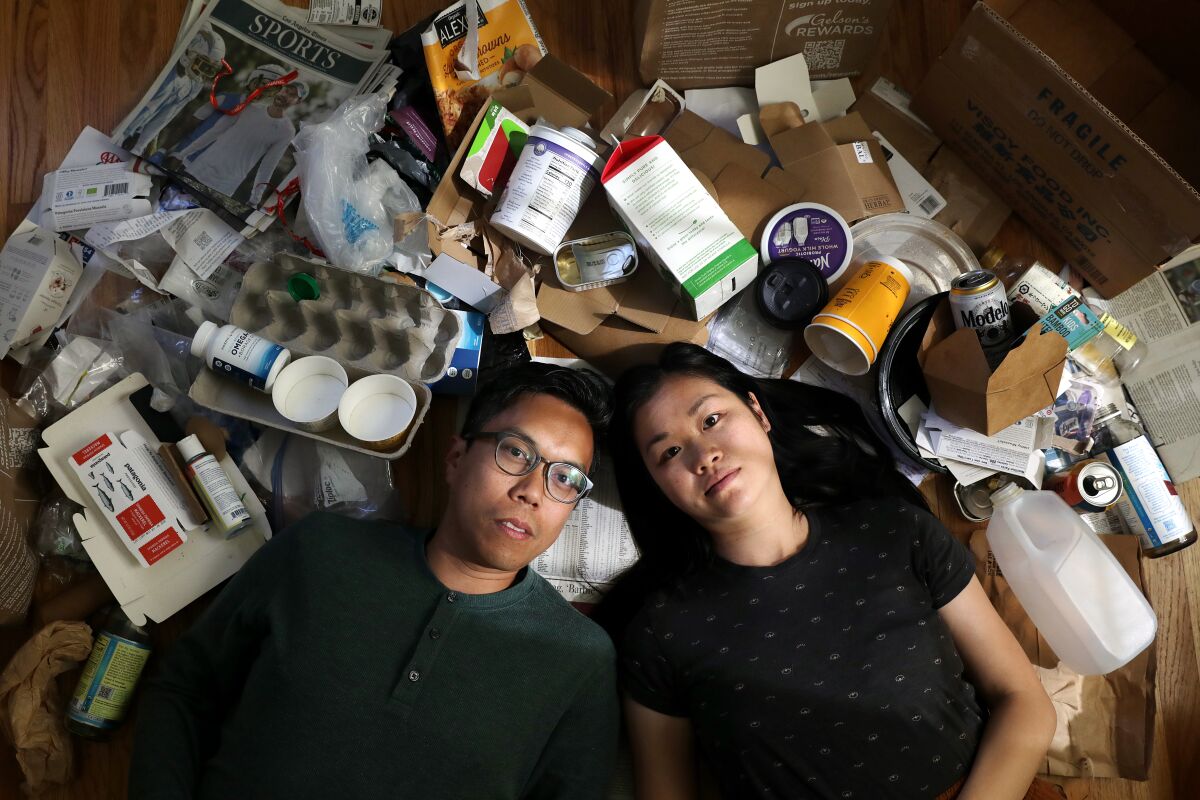 Ein Paar legt sich in seinem Haus inmitten eines Meers aus wiederverwertbarem und nicht wiederverwertbarem Müll nieder.