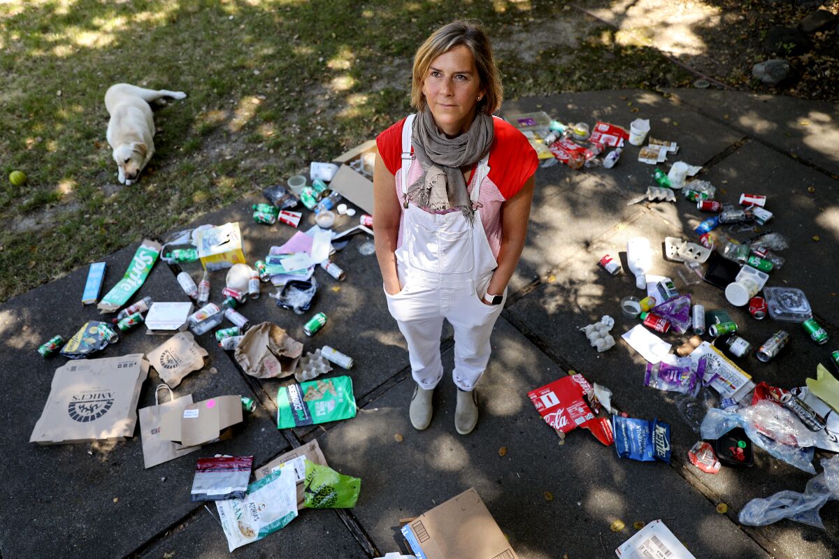 Susanne Rust in weißen Overalls steht inmitten von Müll, der vor ihrem Haus auf dem Boden verstreut ist.