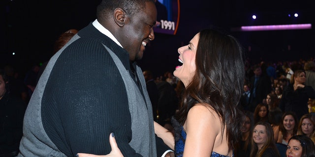 Quinton Aaron schaut auf Sandra Bullock herab, während sie seine Arme packt und über die People's Choice Awards lacht