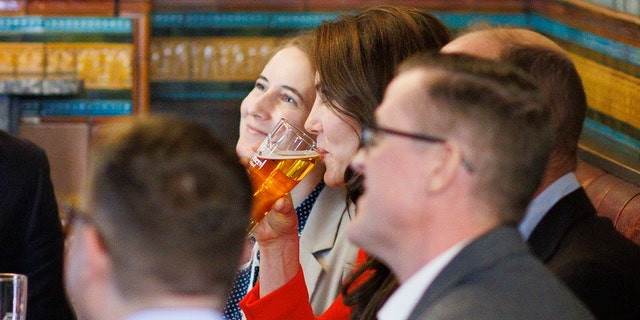 Kate Middleton trägt ein rotes Kleid und trinkt ein Bier