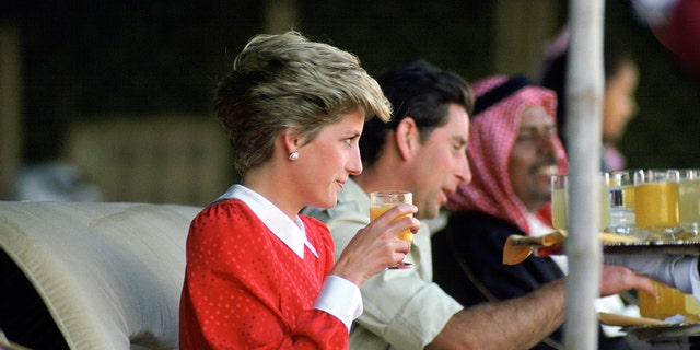 Prinzessin Diana trägt ein rot-weißes Kleid und trinkt neben Prinz Charles