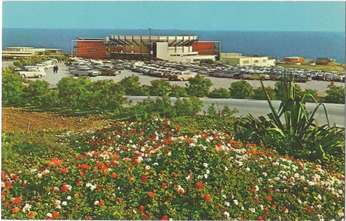 Außenansicht des Marineland und der Parkplätze, umrahmt von Blumen, mit dem Meer im Hintergrund.