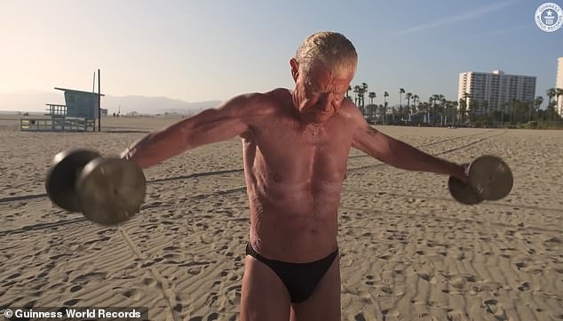 Er ist oben beim Gewichtheben an einem Strand in Los Angeles, Kalifornien abgebildet
