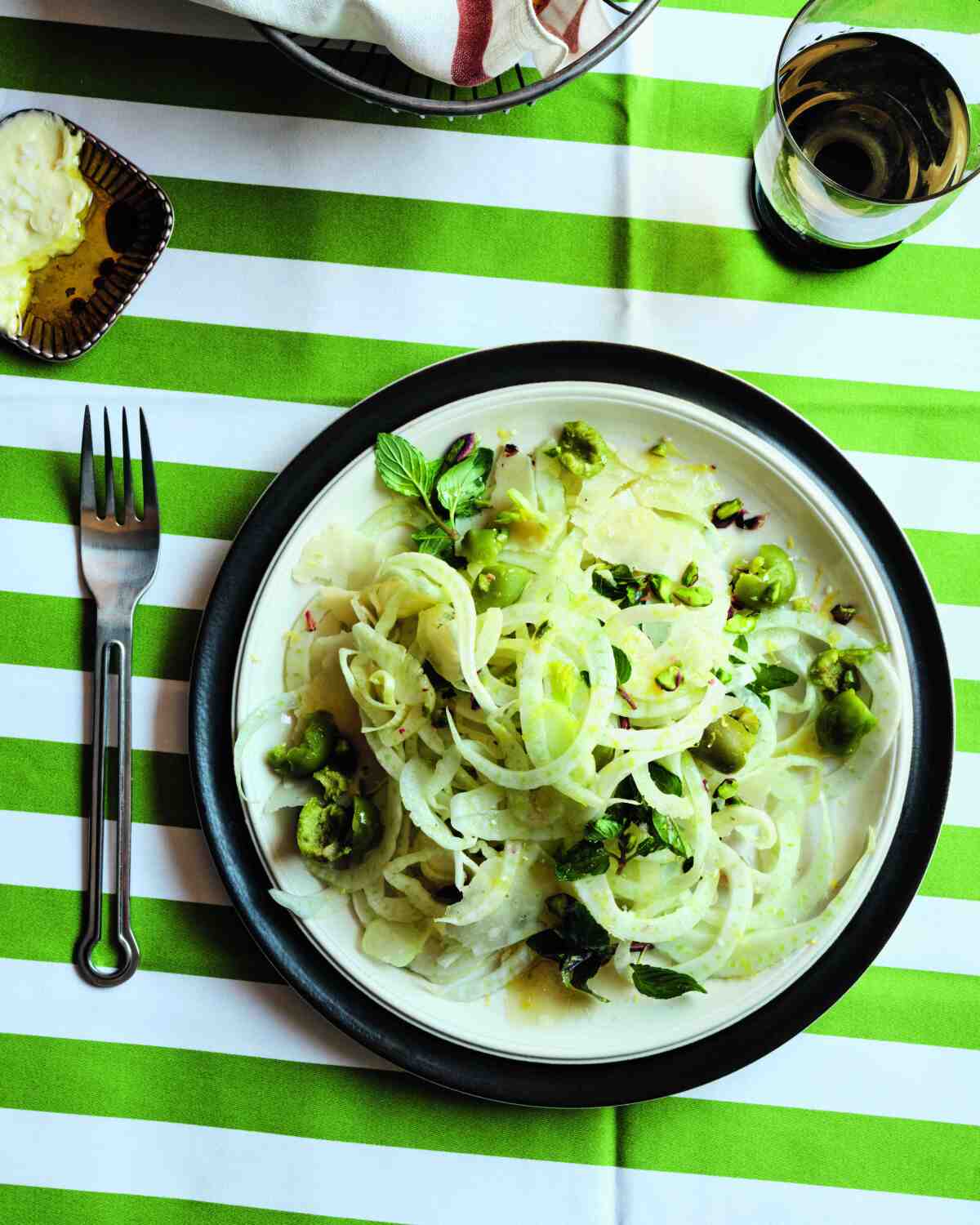 Fenchelsalat mit würzigen grünen Oliven und zerstoßenen Pistazien auf einem Teller auf einer grün-weiß gestreiften Tischdecke