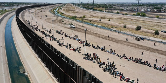 Migranten warten entlang der Grenzmauer