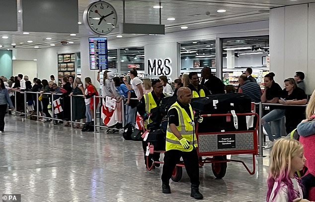 Airport workers move luggage as England fans await the team at Heathrow this morning