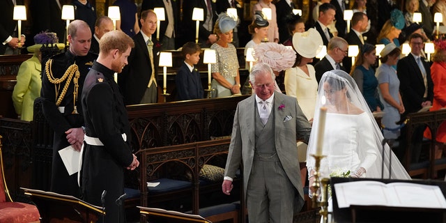 König Charles in einem grauen Anzug führt Meghan Markle in einem Brautkleid zum Altar