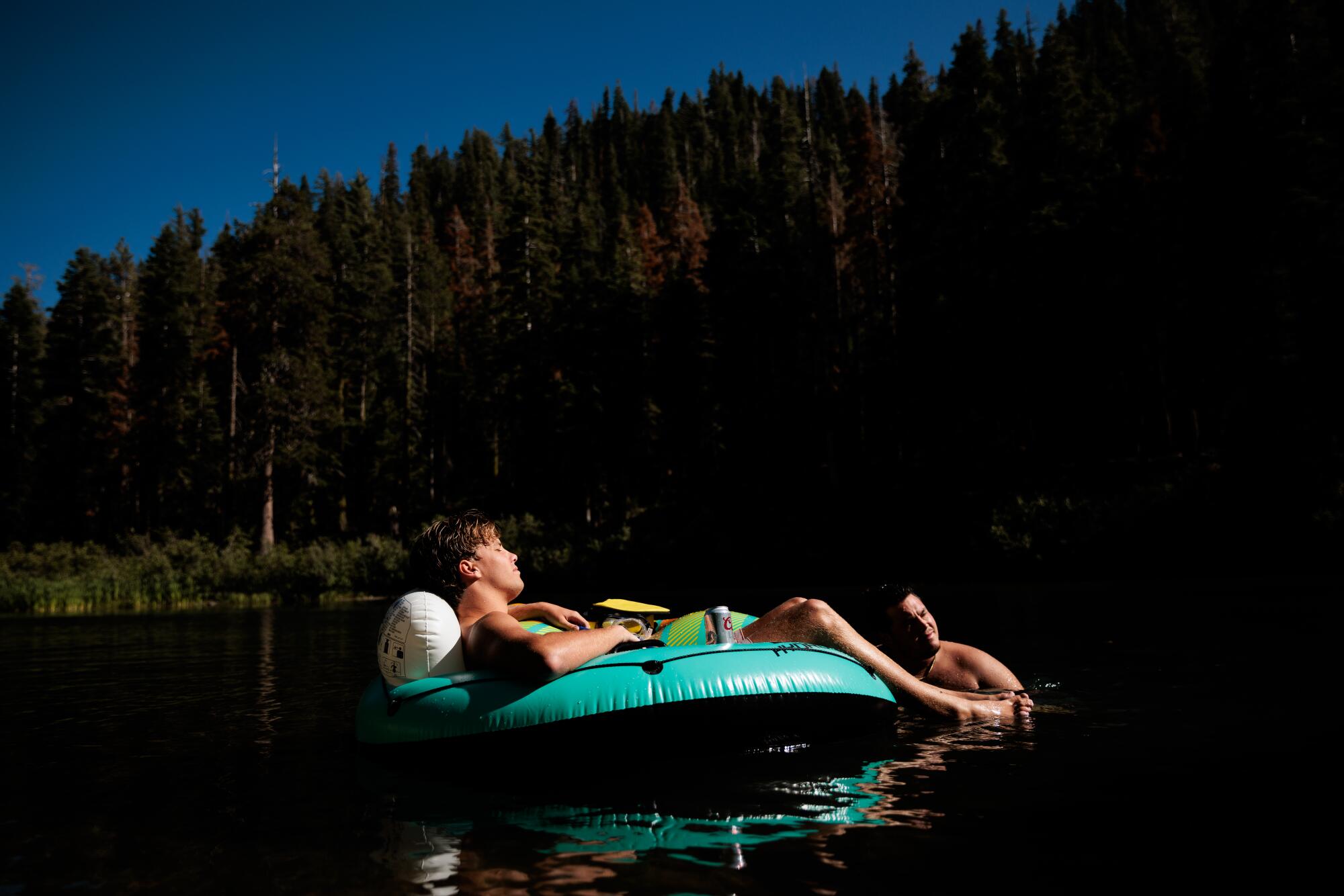 Zwei Menschen mit einem Schlauch auf einem von Nadelbäumen umgebenen See.