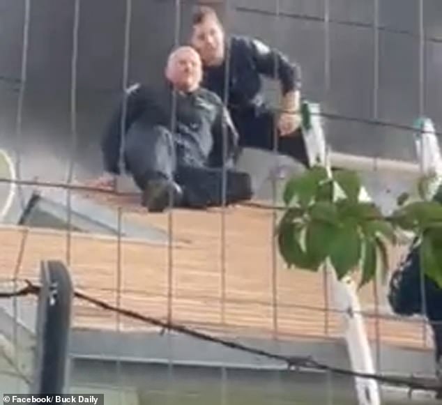 Man sieht zwei Männer in Luftschutzkleidung, die vor den Flammen auf dem Dach des Gebäudes davonkriechen, bevor sie von den Behörden gerettet werden und eine Leiter hinunterklettern
