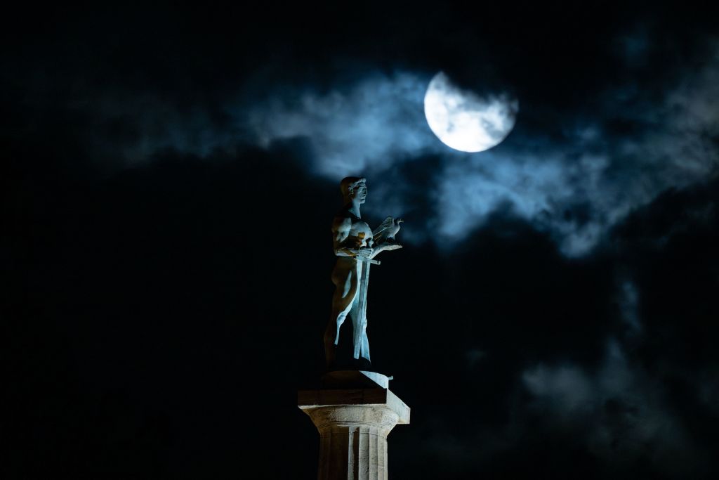 Der superblaue Mond wird in diesem stimmungsvollen Bild, das zeigt, wie er sich über einem Denkmal einer Person erhebt, die auf einer hohen Säule steht, teilweise von Wolken verdeckt.