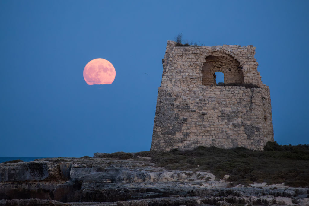 Der superblaue Mond auf der linken Seite leuchtet in einem rosa Farbton neben einem Steinturm mit einer kleinen Öffnung an der Spitze.