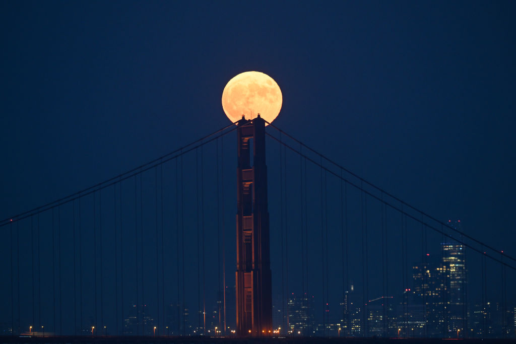 Der helle Vollmond scheint über der Mittelsäule der Golden Gate Bridge, mit der Skyline der Stadt im Hintergrund.