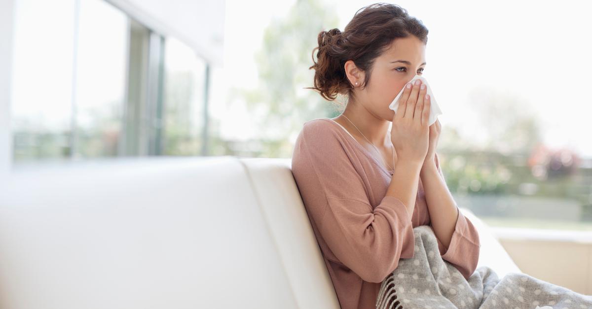 Eine kranke Frau putzt sich die Nase und sitzt auf einer Couch
