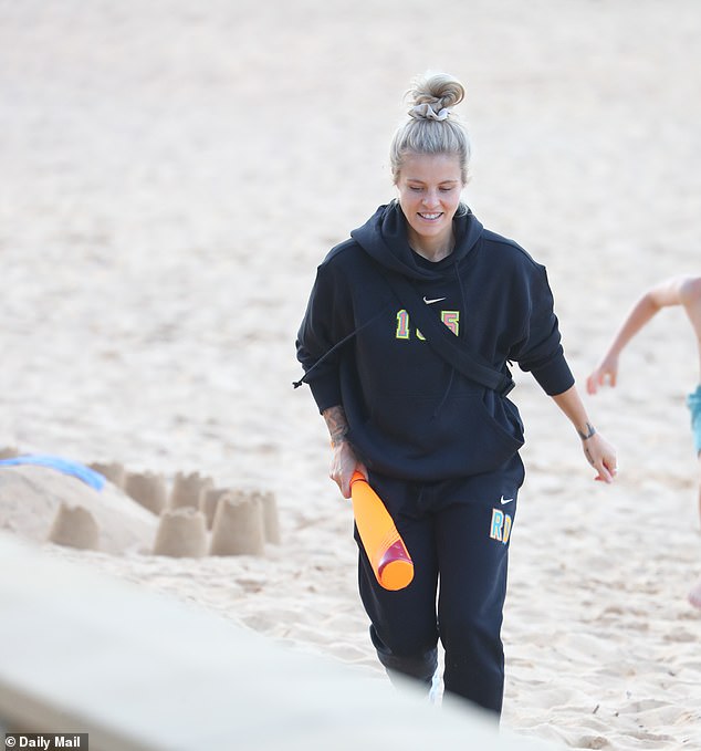 Die Engländerin Rachel Daly lächelt heute an einem Strand in Australien und hält einen orangefarbenen Schläger in der Hand