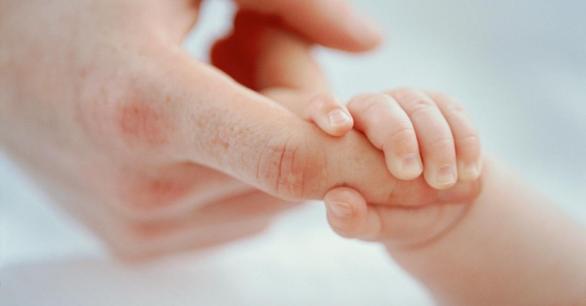 Die Hand eines Babys hält den Finger eines Mannes.