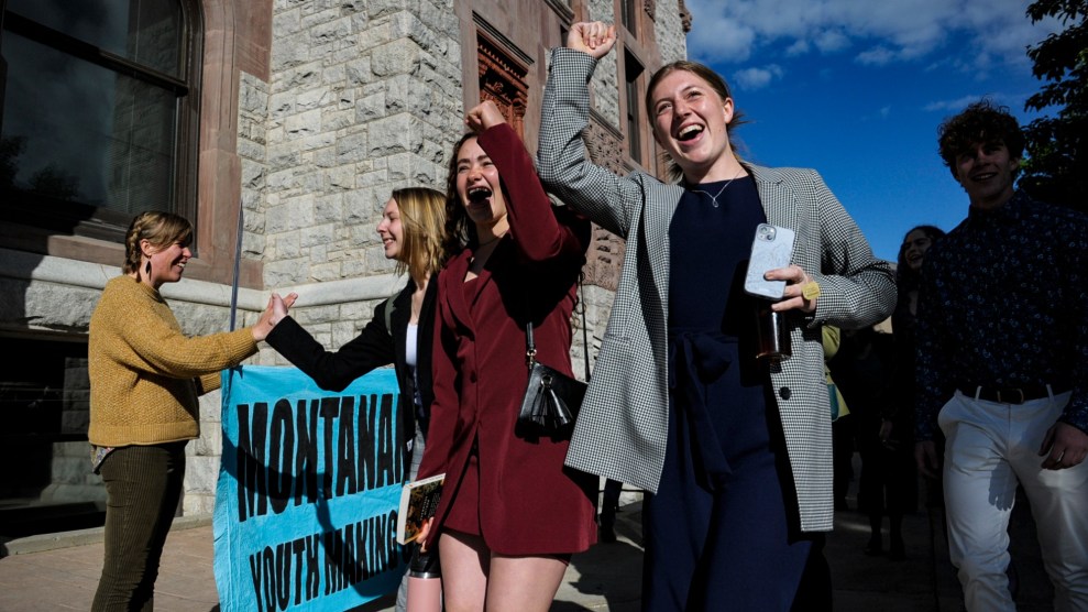 Zwei weiße Jugendliche heben jubelnd die Fäuste in die Luft.  Sie stehen neben einem leuchtend blauen Schild, auf dem teilweise zu lesen ist "Montana-Jugendbildung." Im Hintergrund geben andere High Fives.