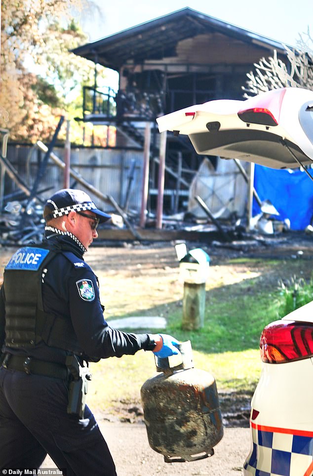 Auf dem Foto ist ein Polizist zu sehen, der einen Gaskanister vom Ort eines tragischen Brandes in Queensland mitnimmt