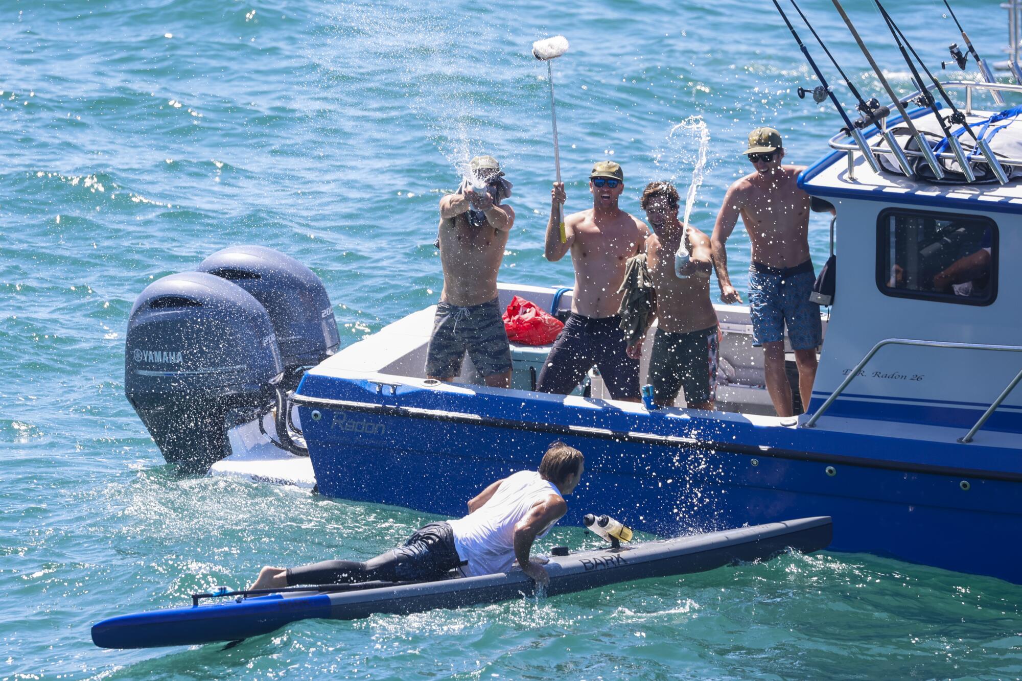 Jake Miller auf seinem Paddleboard wird von seinem Team auf einem Boot beglückwünscht