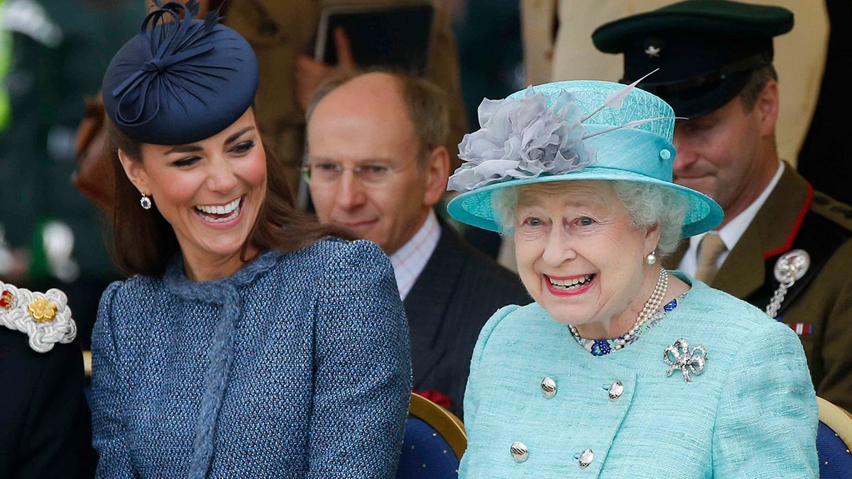 Eine Nahaufnahme von Kate Middleton in einem dunkelblauen Anzug, die neben einer lächelnden Königin Elizabeth in einem leuchtend hellblauen Anzug sitzt