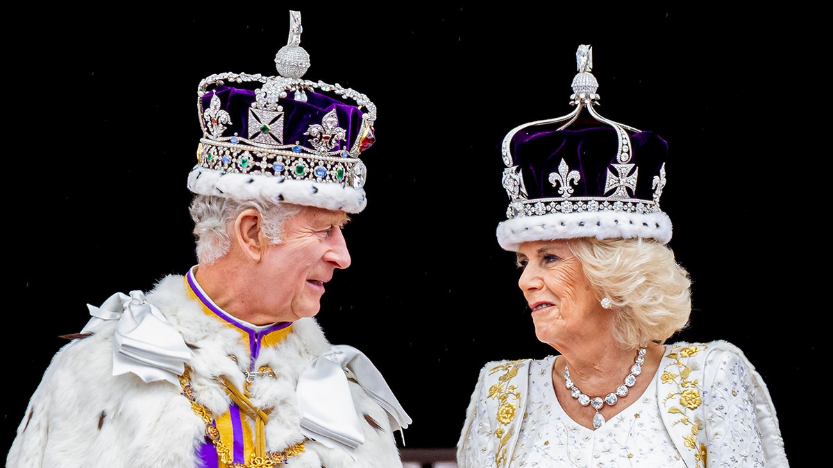 König Charles in seinem königlichen Ornat blickt Camilla in einem weißen Kleid mit einer Krone an