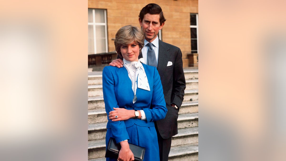 Prinzessin Diana trägt ein blau-weißes Kleid und steht vor Prinz Charles im grauen Anzug
