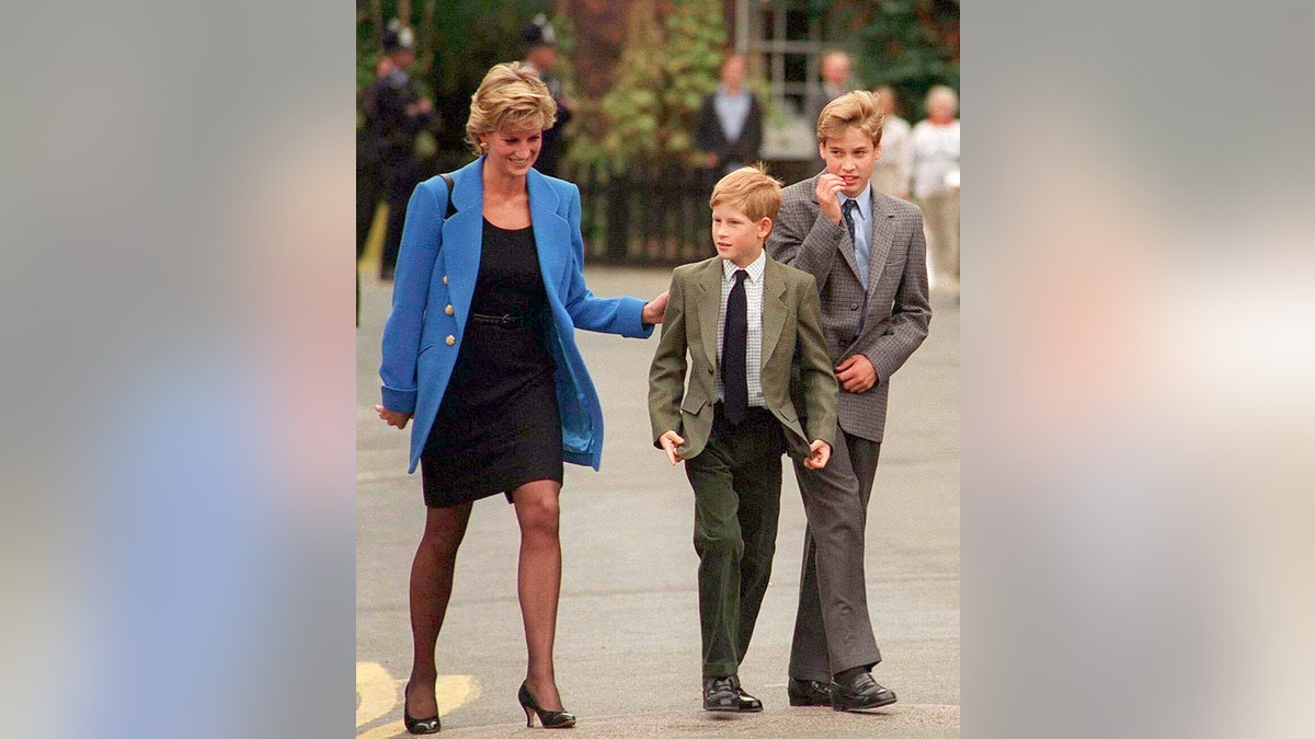 Prinzessin Diana trägt ein schwarzes Kleid und einen blauen Blazer und läuft neben ihren beiden kleinen Söhnen