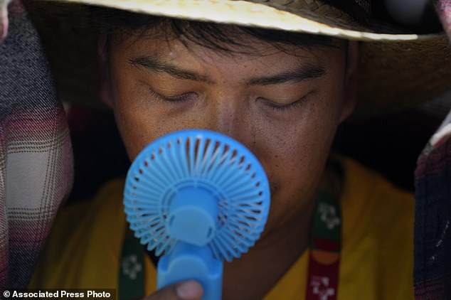 A man uses a small fan to cool off from the intense heat at Passeio Marítimo in Algés, just outside Lisbon, Portugal, August 6, 2023