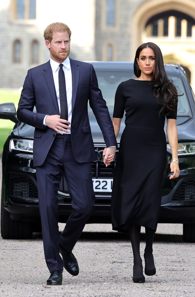 Prinz Harry und Meghan Markle halten Händchen und sehen düster aus, gekleidet in Schwarz und gehen vor einem Auto