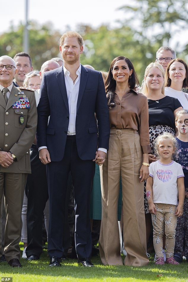 The royal couple hold hands as they pose for pictures. Meghan wore loose fitting wide leg caramel coloured trousers and a silky brown shirt. Harry wore a blue suit but no tie