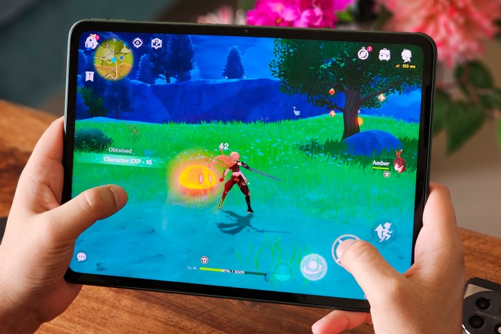 Genshin Impact läuft auf dem OnePlus Pad mit einem Holztisch und Kunstblumen im Hintergrund.