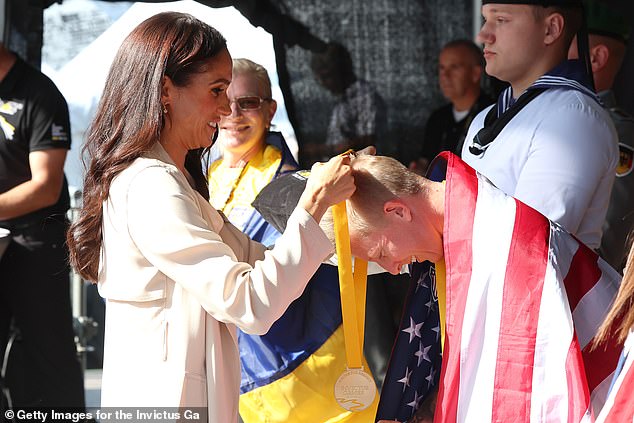 Meghan Markle hugged an athlete draped in the American flag as she took centre stage on the final day of the Invictus Games today